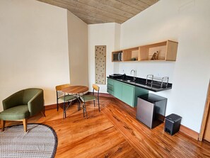 Ein kompakter Wohnraum mit Holzboden, einem Esstisch mit Stühlen, einer Küchenzeile mit Spüle und Schränken sowie einer kleinen Mülltonne.