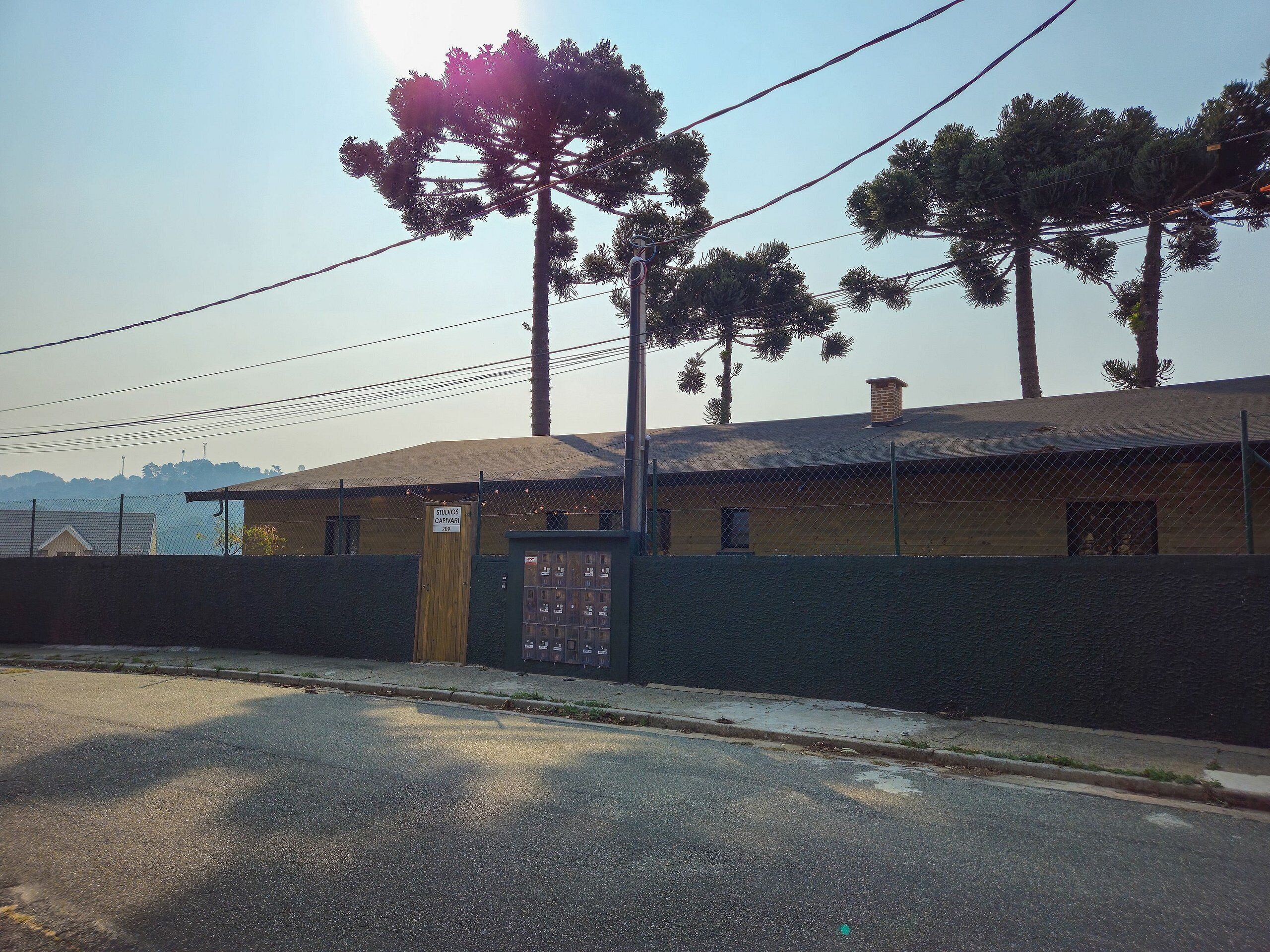 A building with a fenced exterior, a sign indicating 'STUDIOS CAPAVARI 2019', and a clear sky.