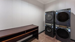 A laundry room with two stacked front-loading washing machines and a wooden bench. - Post And Telecommunication Mansion (Taiyuan)