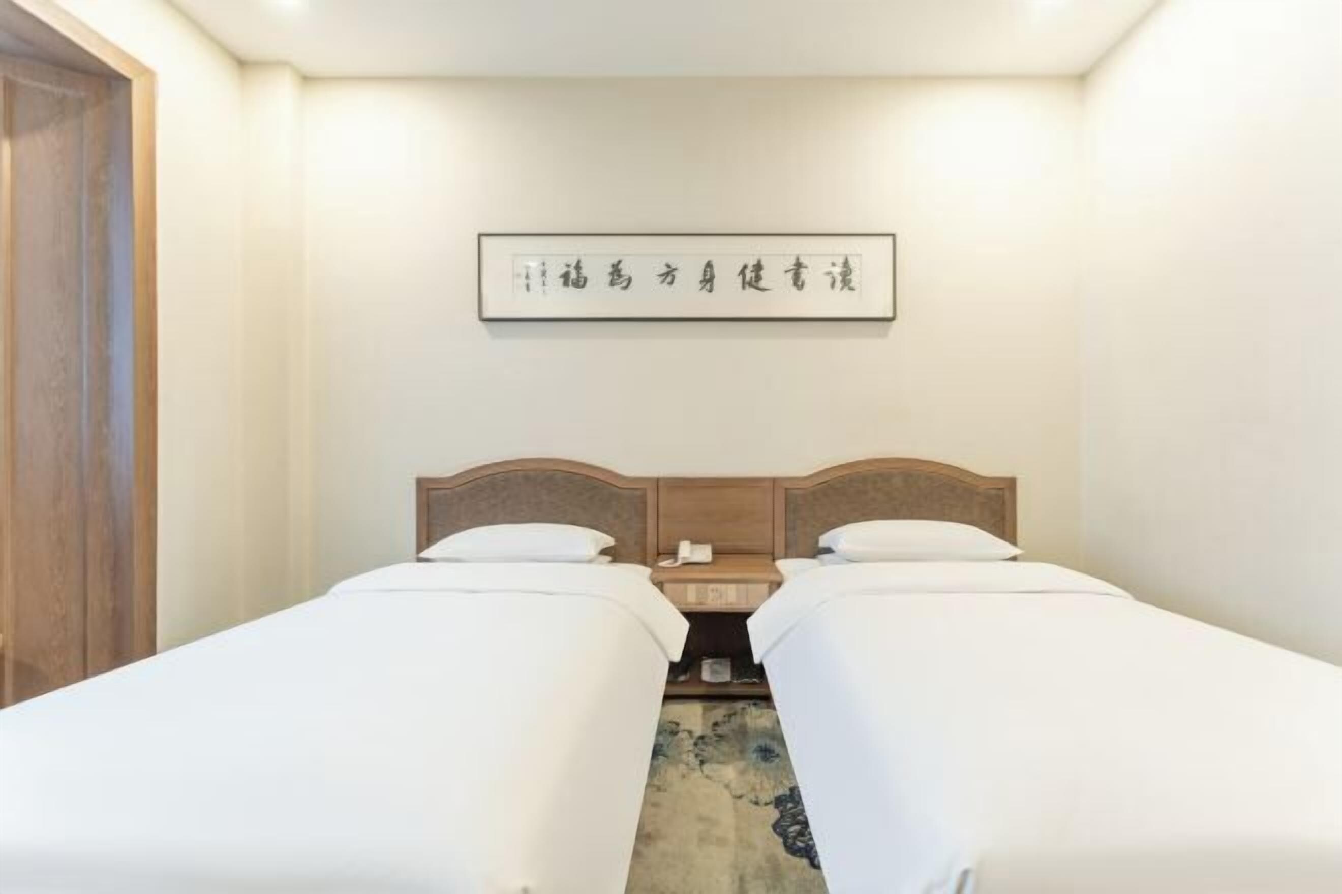 Une chambre d’hôtel avec deux lits, une tête de lit en bois, une table de chevet avec un téléphone et un panneau fixé au mur.