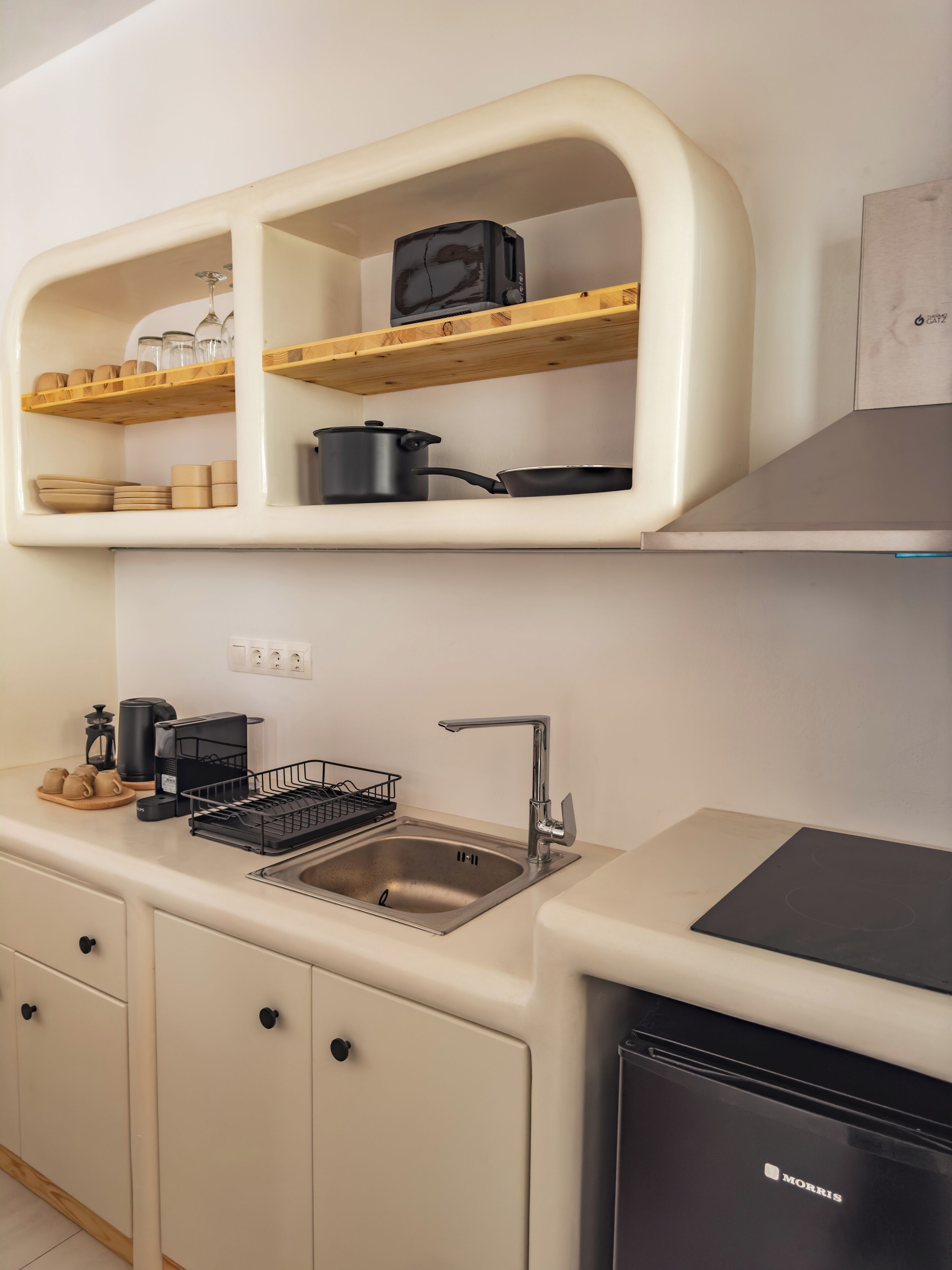 A compact kitchen with a sink, a stove, and wooden shelves above.