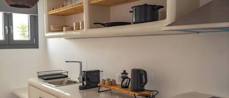 A modern kitchen with white cabinetry, a black refrigerator, and wooden shelves above the counter.