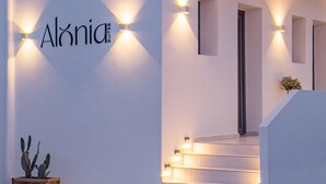 Ένα σύγχρονο κτίριο με μινιμαλιστικό σχεδιασμό, που διαθέτει μια σκάλα που οδηγεί στην είσοδο, ένα φυτό κάκτο και φωτιστικά τοίχου.