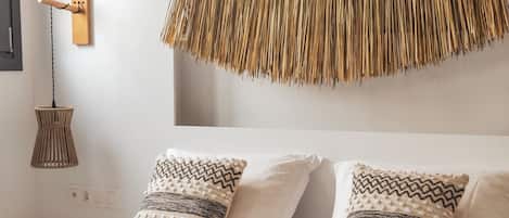 A bed with patterned pillows, a woven wall hanging, and a hanging light fixture.