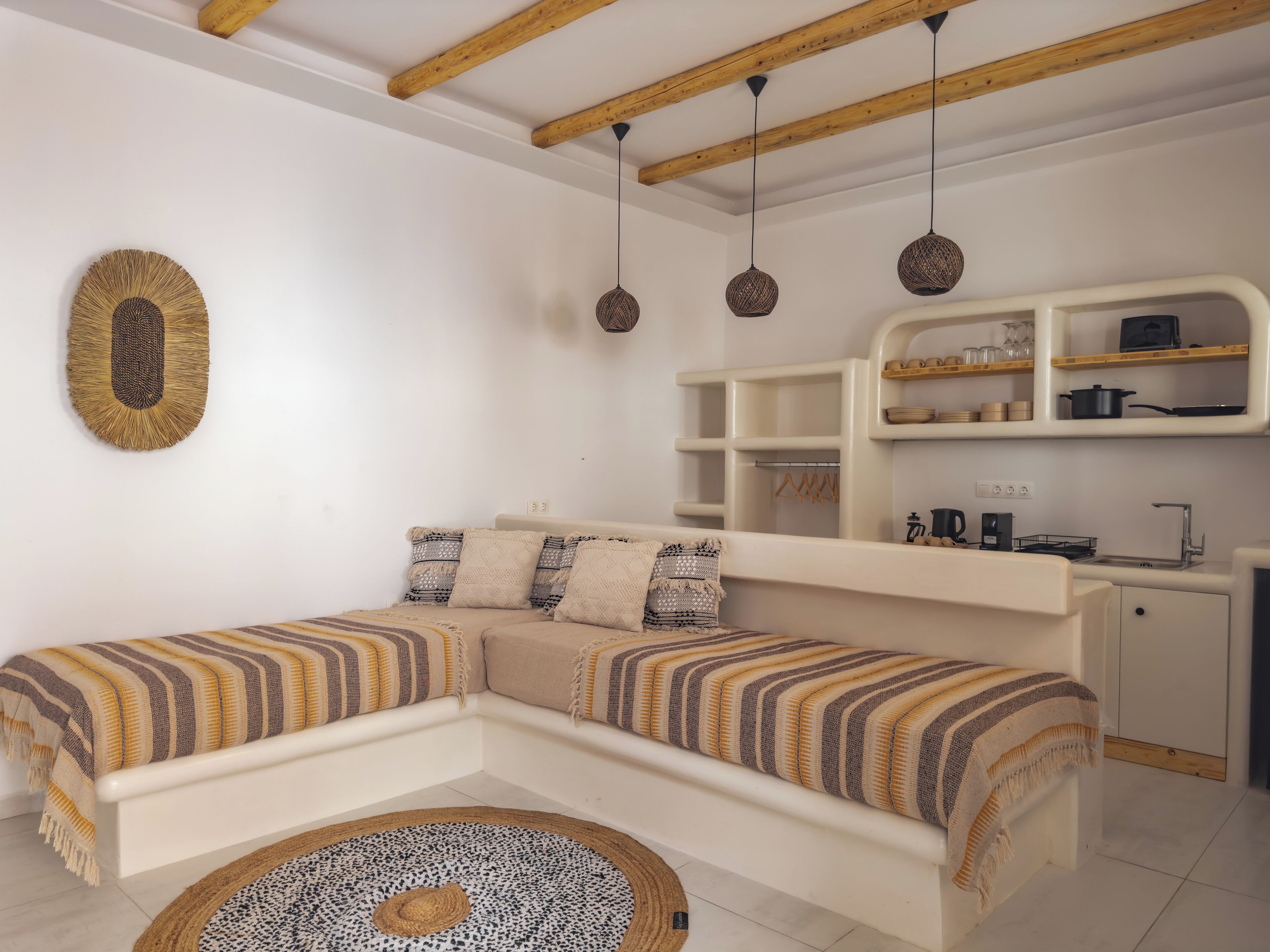 Una sala de estar moderna con un sofá blanco, un tapete redondo y una zona de cocina con armarios blancos y estantes de madera.