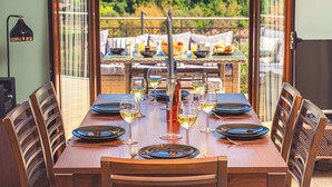 Une table à manger dressée pour six personnes, avec des verres à vin, des assiettes et des couverts, donnant sur un jardin.