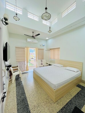 A hotel room with a large bed, a desk with a chair, a ceiling fan, and a TV. - Maganlal Mehta Bhavan (Tarangambadi)