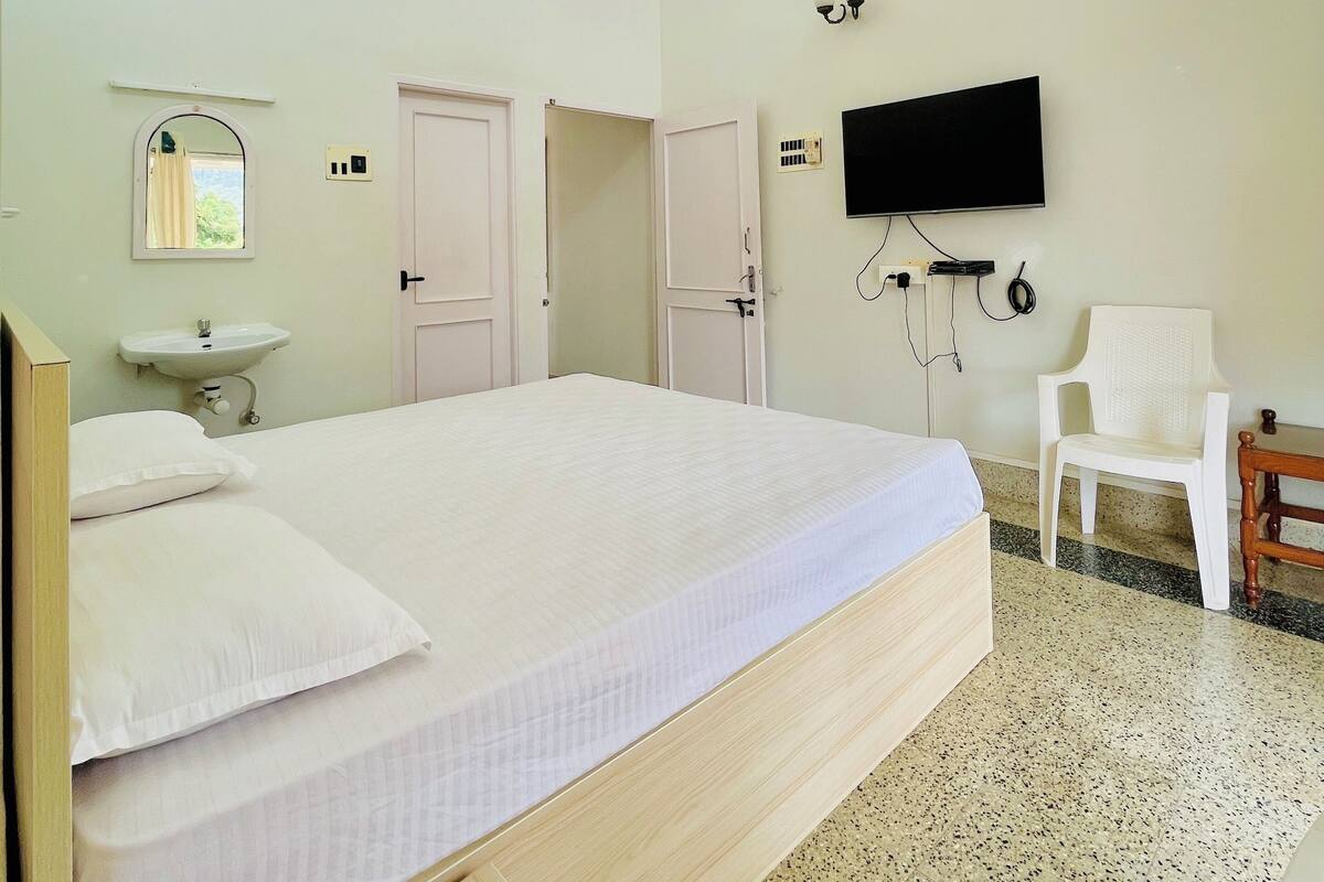 Ein Schlafzimmer mit einem großen Bett, einem Deckenventilator, einem Fernseher, einem Sessel und einem Fenster.
