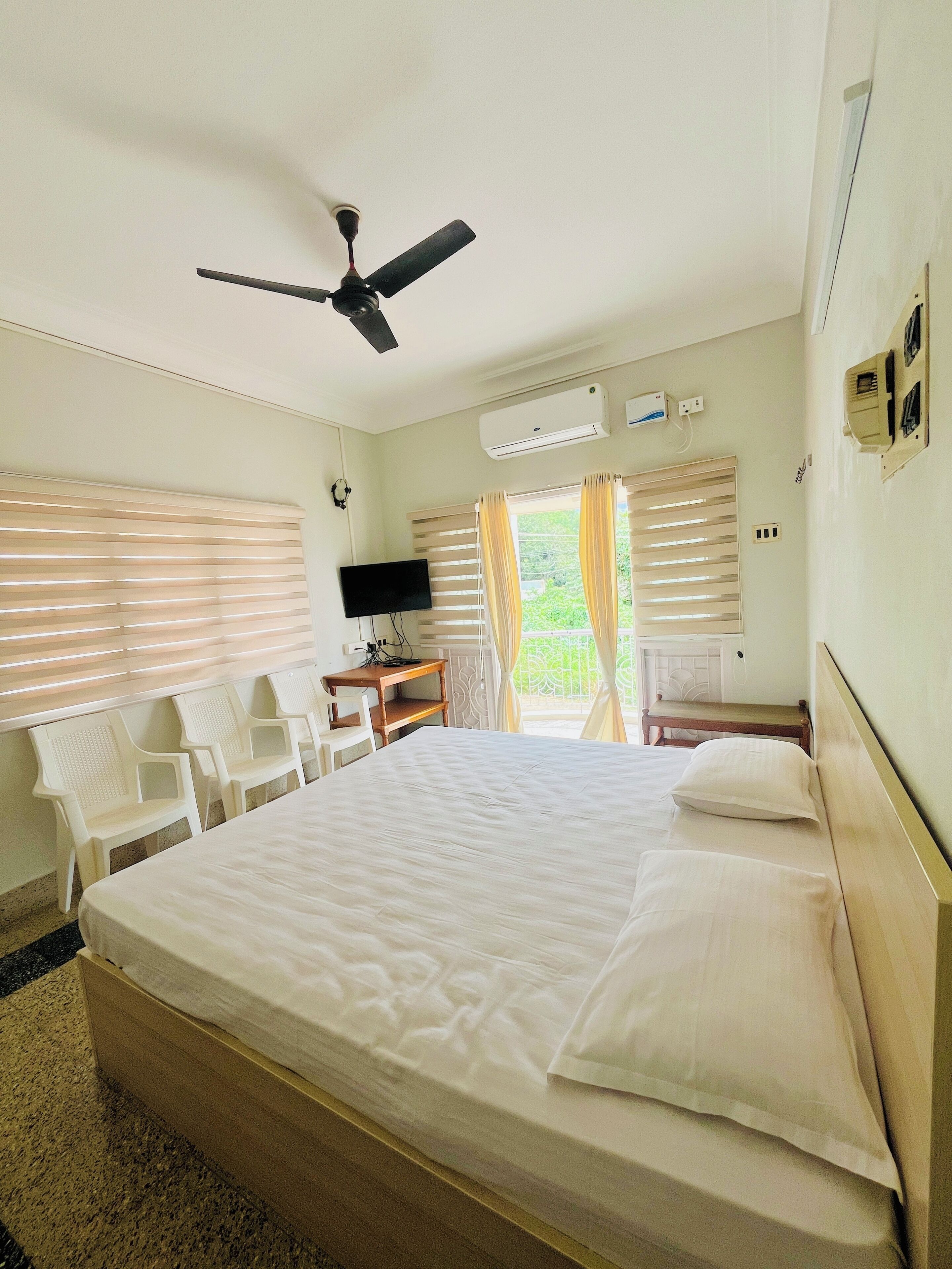 A hotel room with a large bed, a ceiling fan, a TV, and a desk with chairs.