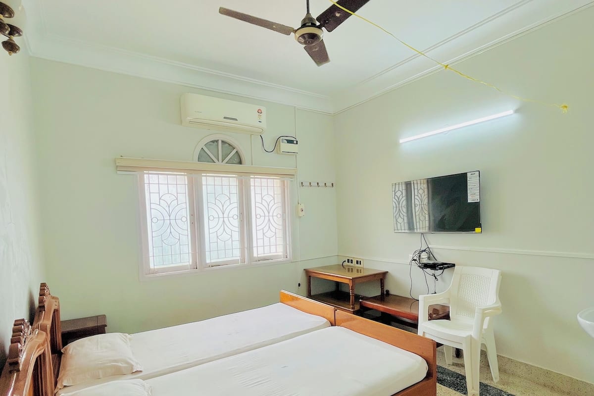 Ein Zimmer mit zwei Holzbetten, einem Deckenventilator, einer Klimaanlage, einem Fernseher, einem Schreibtisch und einem Stuhl.
