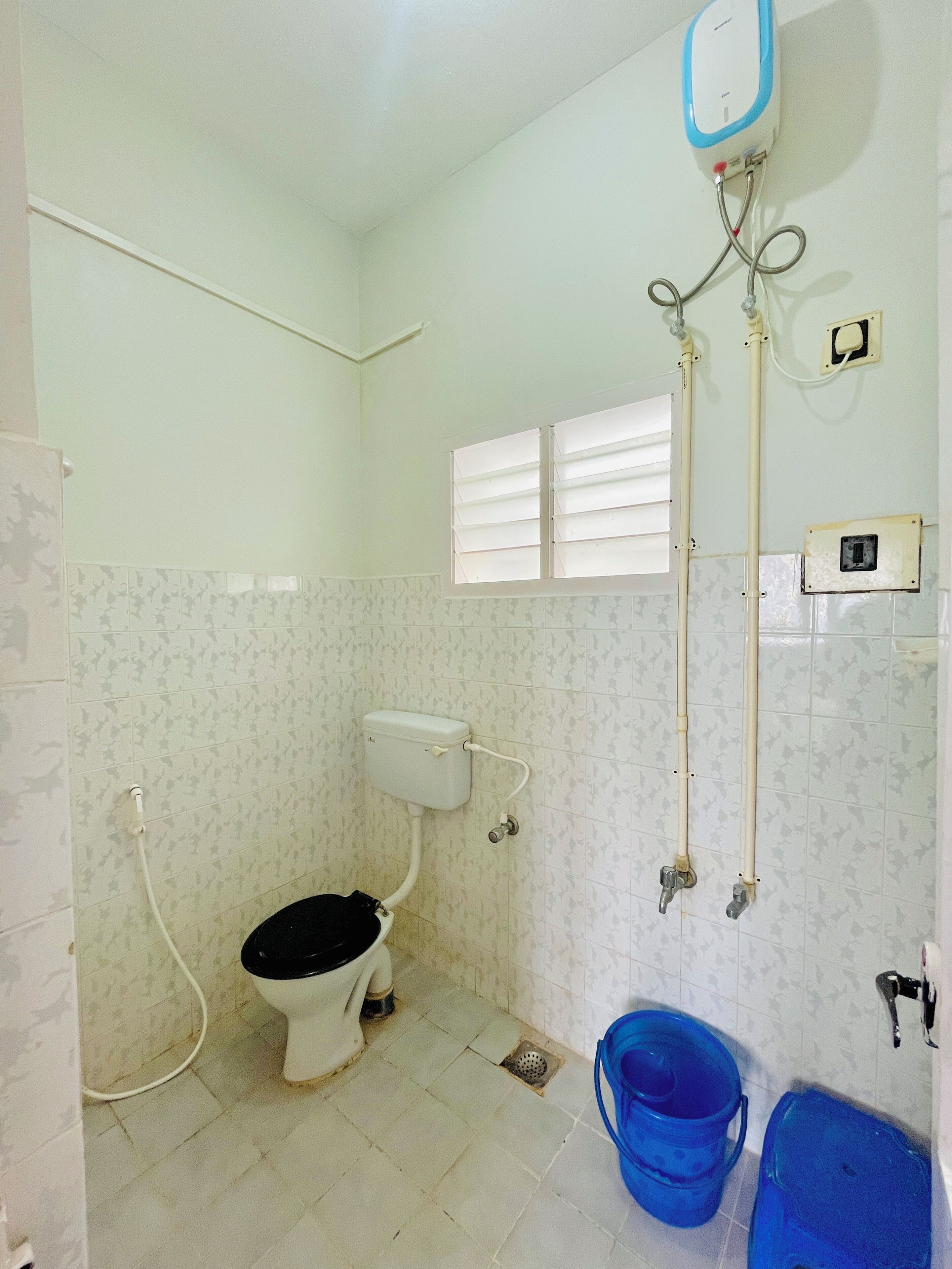 A small bathroom with a toilet, a bidet, a window, and a blue bucket.