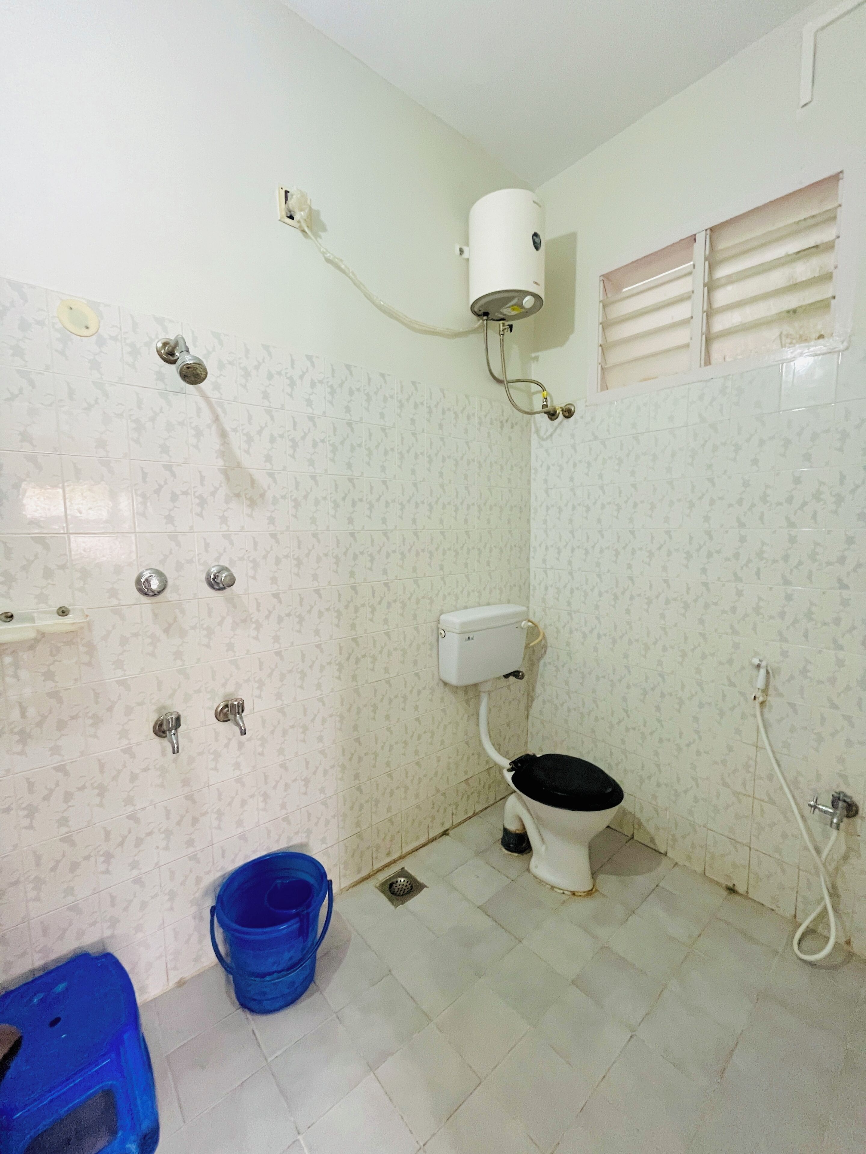A small bathroom with a toilet, a shower head, and a blue bucket.