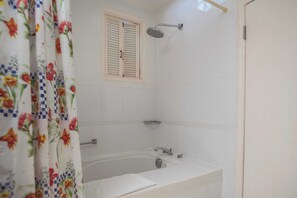 A bathroom with a bathtub, a showerhead, and a window with shutters. - One Bedroom Suite at Mystic Ridge (Ocho Rios)