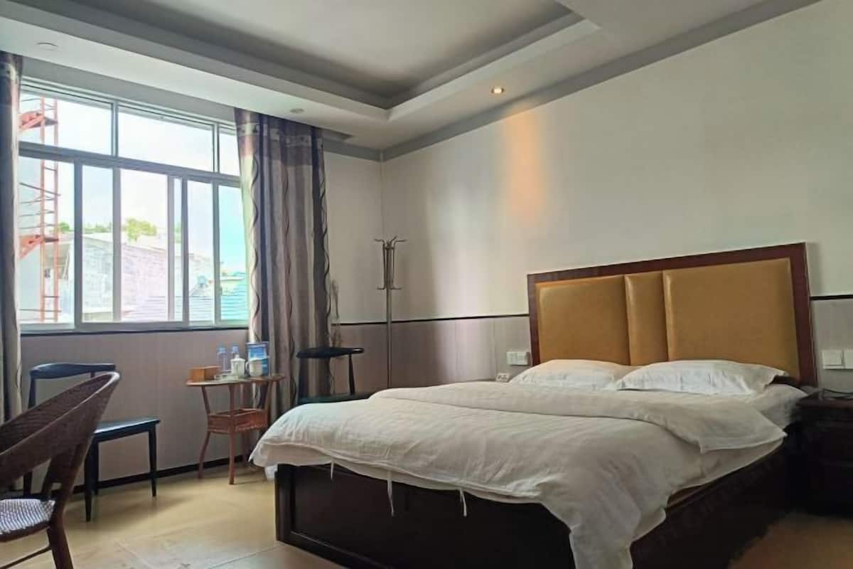 Ein Hotelzimmer mit Bett, Sessel, kleinem Tisch mit Lampe und Fenster mit Vorhängen.