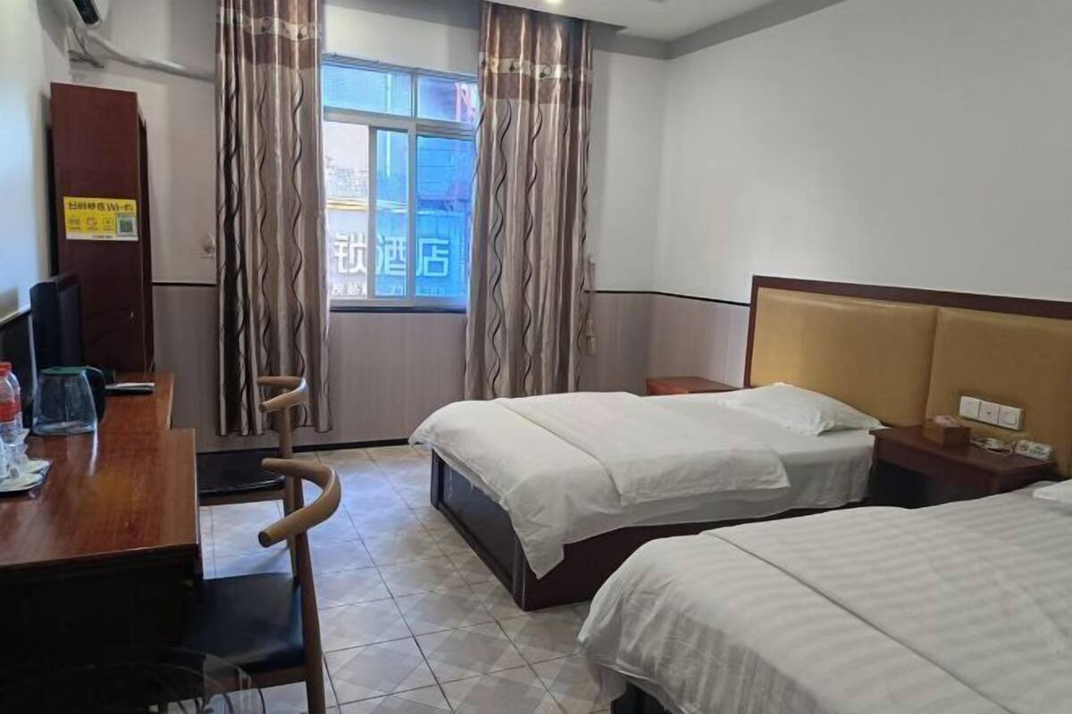 Ein Hotelzimmer mit zwei Betten, einem Schreibtisch mit Stuhl, einem kleinen Tisch und einem Fenster mit Vorhängen.