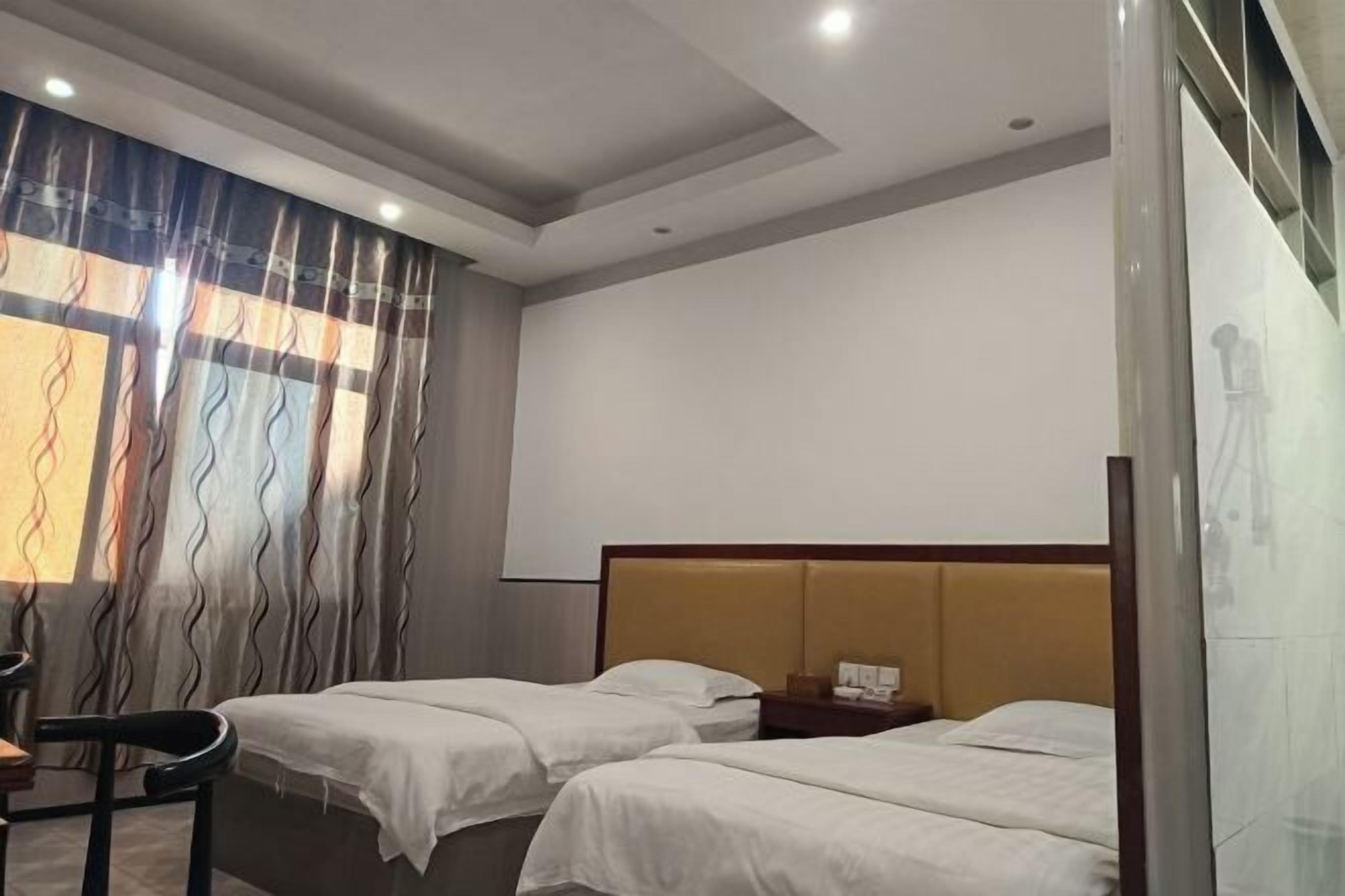 Habitación de hotel con dos camas, cabecera de madera, escritorio con silla y una ventana grande con cortinas.