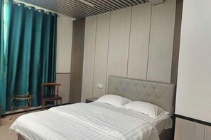 A bedroom with a bed, a nightstand, a chair, and a window with curtains.