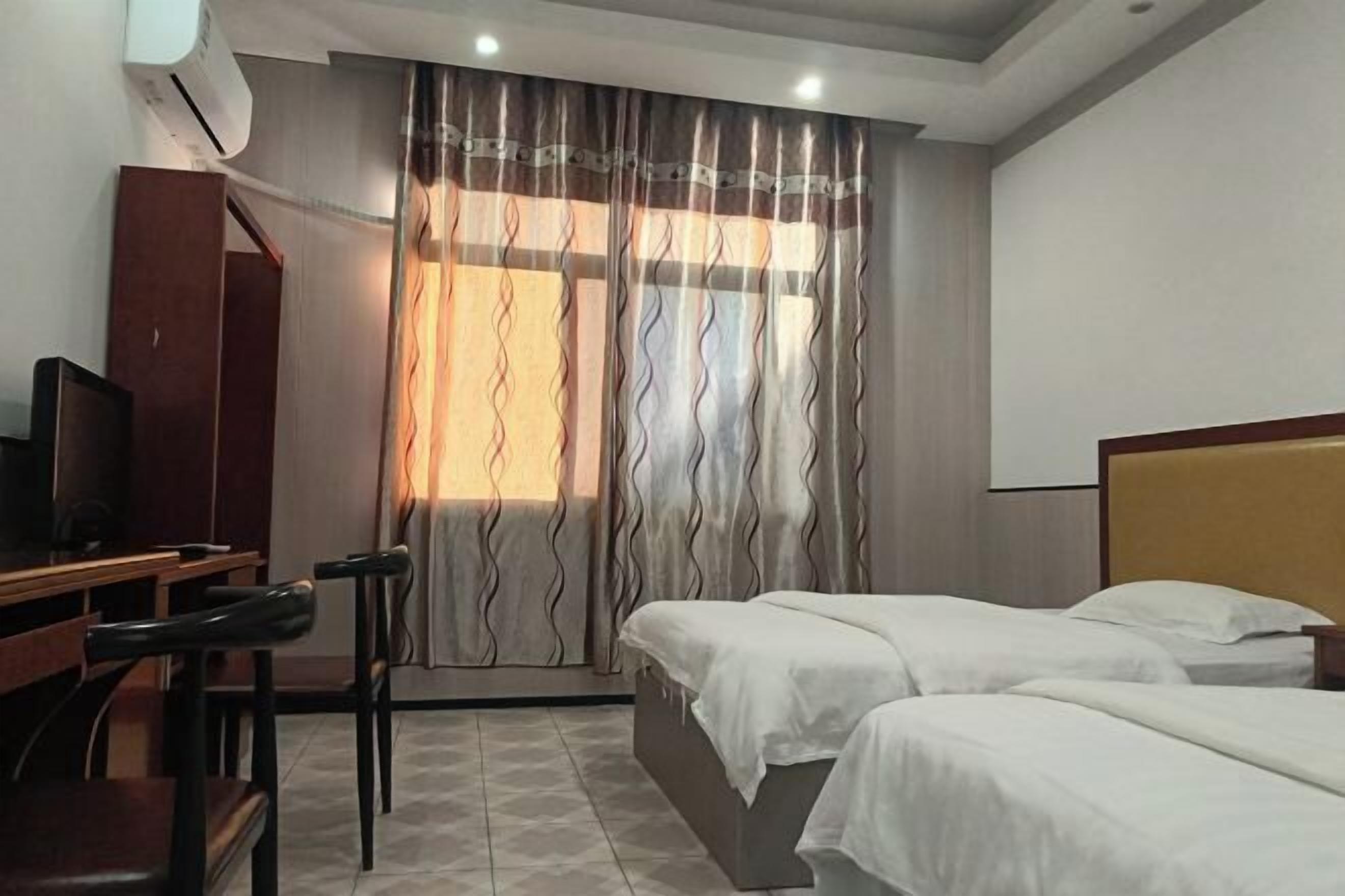 A hotel room with two beds, a desk with a chair, a television, and a window with curtains.