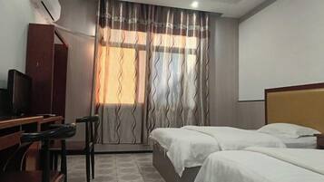 A hotel room with two beds, a desk with a chair, a television, and a window with curtains.