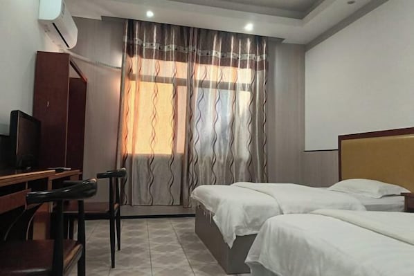 A hotel room with two beds, a desk with a chair, a television, and a window with curtains.