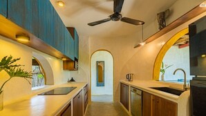 A narrow kitchen with wooden cabinets, a black countertop, and a ceiling fan. - Flow House 3BR Oceanview An Bang Beach  (Da Nang)
