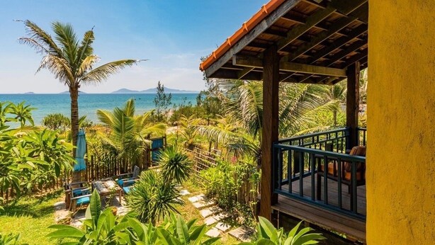A tropical resort with a wooden deck overlooking a palm-lined beach and the ocean. - Flow House 3BR Oceanview An Bang Beach  (Da Nang)