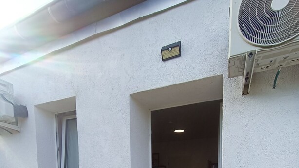 Un'area relax esterna con due sedie blu e un tavolo, una finestra con una pianta in vaso rosso e un condizionatore d'aria montato a parete.