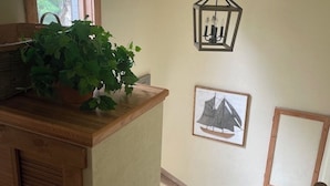 Una escalera con barandilla de madera y escalones alfombrados, una planta en maceta sobre una encimera de madera, un aplique de pared y un cuadro en la pared.