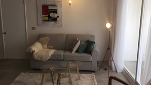 A living room with a grey sofa, a glass coffee table, a floor lamp, and a painting on the wall. - Apartamento Urbano en Santiago (Santiago)