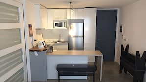 A compact kitchen with a central island, a microwave, and a refrigerator. - Apartamento Urbano en Santiago (Santiago)