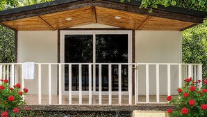 A small, enclosed structure with a wooden roof and white railing, surrounded by lush greenery and red flowers. - Hotel Heaven Stay (Shankarpalle)