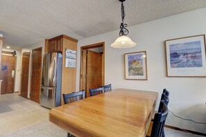 A dining area with a wooden table and chairs, a stainless steel refrigerator, and framed artwork on the wall. - Penthouse in Center Village, Extra Sleeping Area, Amazing views. (Copper Mountain)