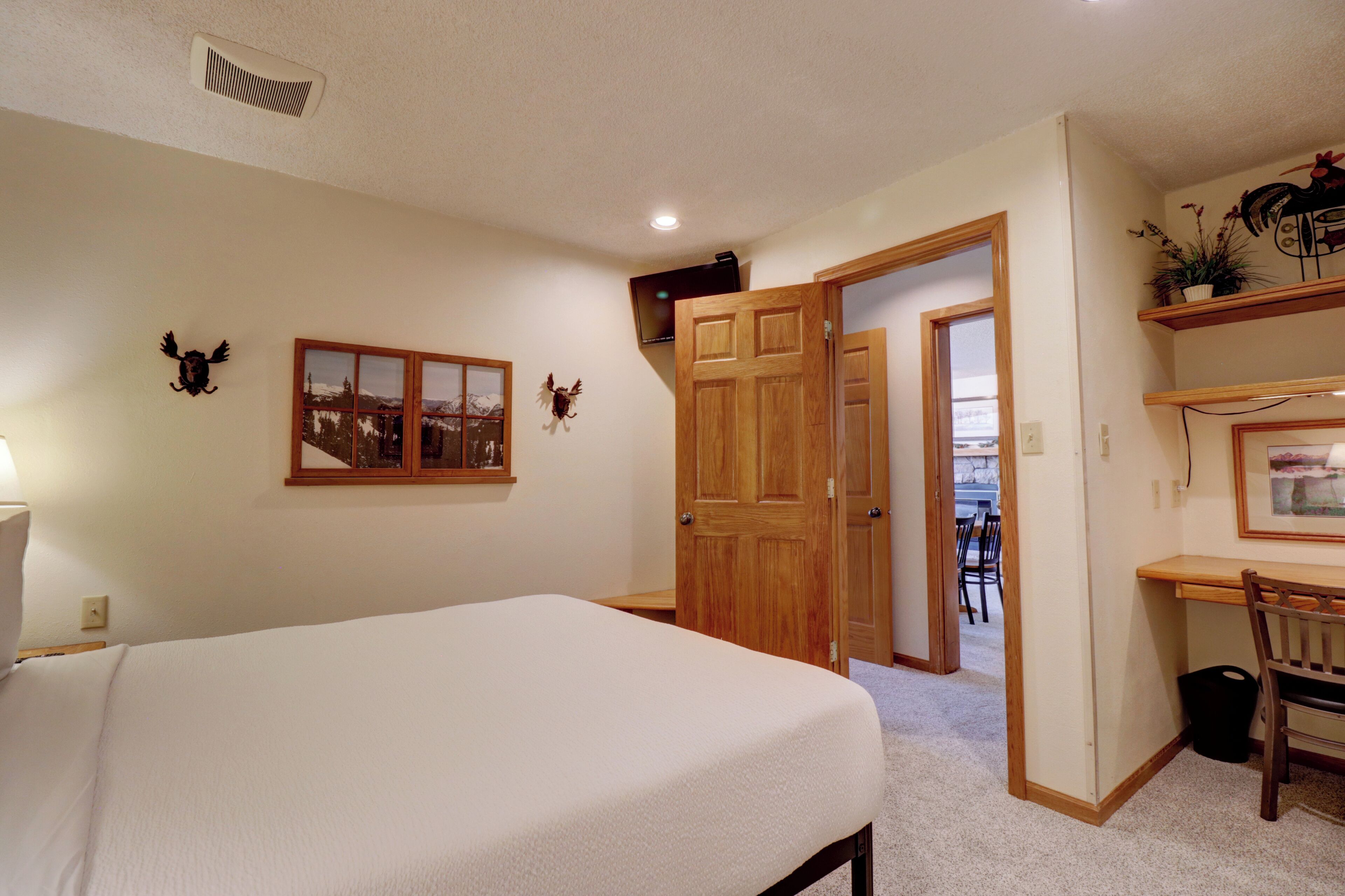 Un dormitorio con una cama, un escritorio y una silla. Hay una puerta que conduce a otra habitación.