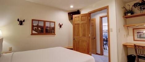 Un dormitorio con una cama, un escritorio y una silla. Hay una puerta que conduce a otra habitación.