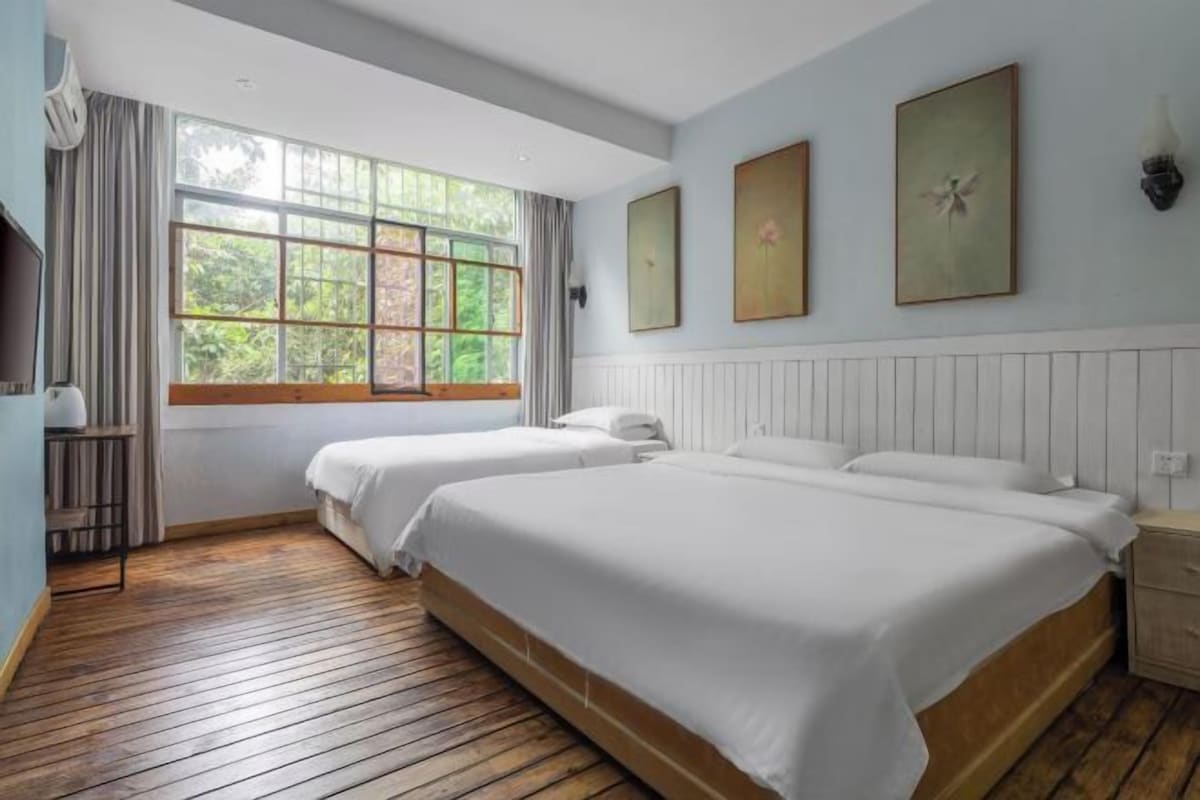 Een hotelkamer met twee bedden, een groot raam met gordijnen en drie ingelijste foto’s aan de muur.