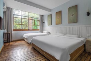 A hotel room with two beds, a large window with curtains, and three framed pictures on the wall.