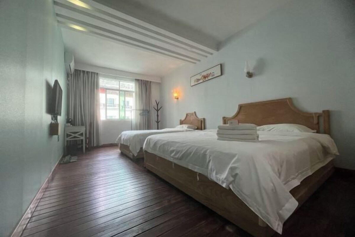 Een hotelkamer met twee bedden, een houten vloer, een raam met gordijnen, een tv aan de muur en een klein tafeltje.