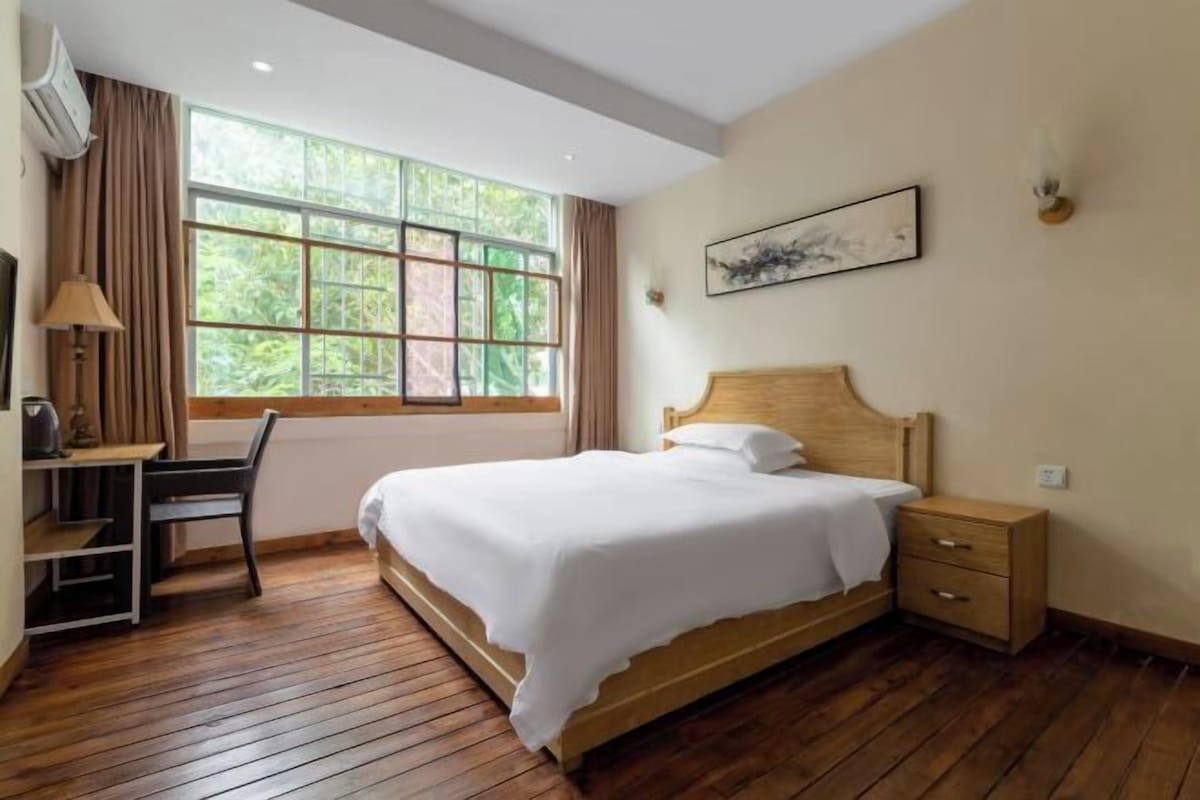 Een slaapkamer met een houten bed, een bureau, een stoel, een nachtkastje en een raam met gordijnen.