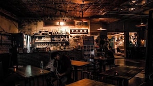 Un bar tenuemente iluminado con mesas de madera y una pared de ladrillo.