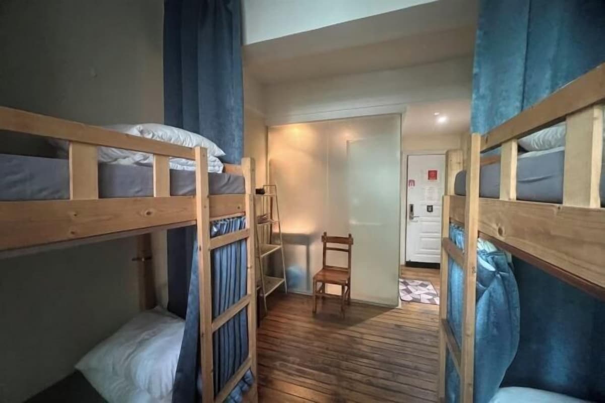 Een slaapkamer met stapelbedden, een houten vloer, een stoel en een deur op de achtergrond.
