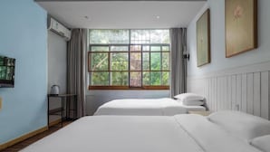 Habitación de hotel con dos camas, una ventana con cortinas, un radiador y un cuadro en la pared.