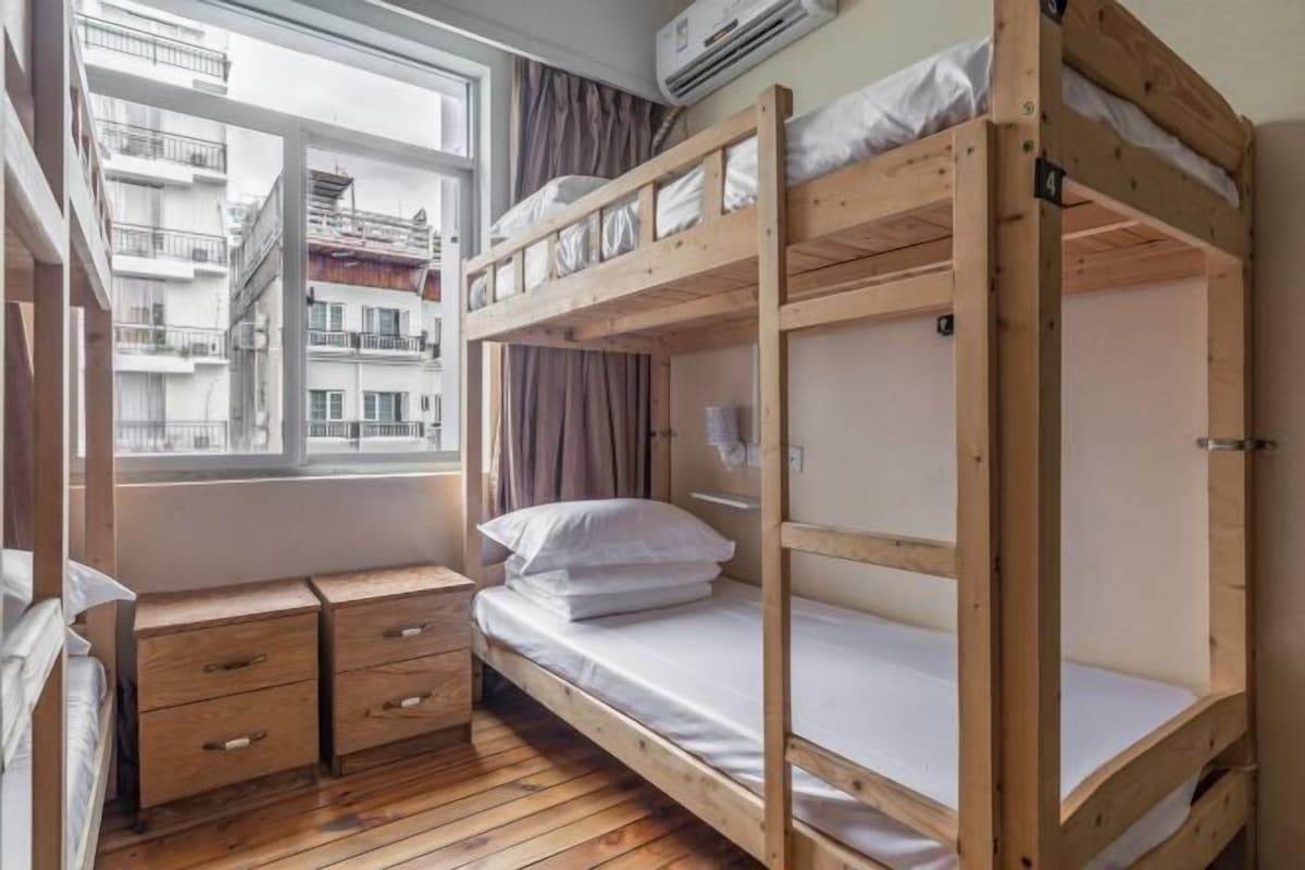 Een slaapkamer met stapelbedden, houten vloeren, een raam met gordijnen en een klein houten bureau met lades.