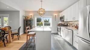 A modern kitchen with a central island, white cabinetry, stainless steel appliances, and a hanging light fixture.