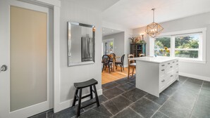 A modern kitchen with a central island, dark tiled flooring, and a dining area with natural light from a large window.