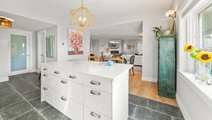 A modern kitchen with a central island, a dining area with wooden chairs, and a large window with a view.