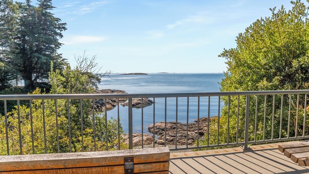 A wooden bench with a plaque, overlooking a rocky shoreline and calm sea under a clear sky.