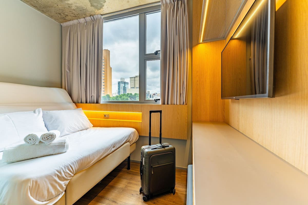 A hotel room with a bed, a suitcase, and a window with curtains.