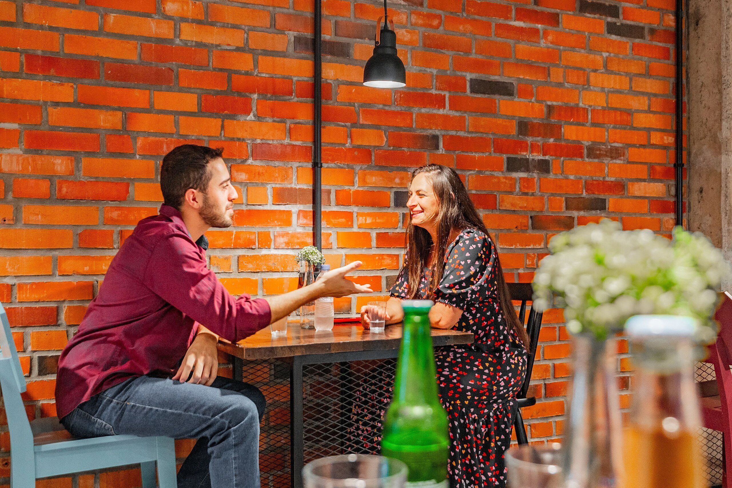 Un hombre y una mujer sentados en una mesa de café, con un muro de ladrillo de fondo.