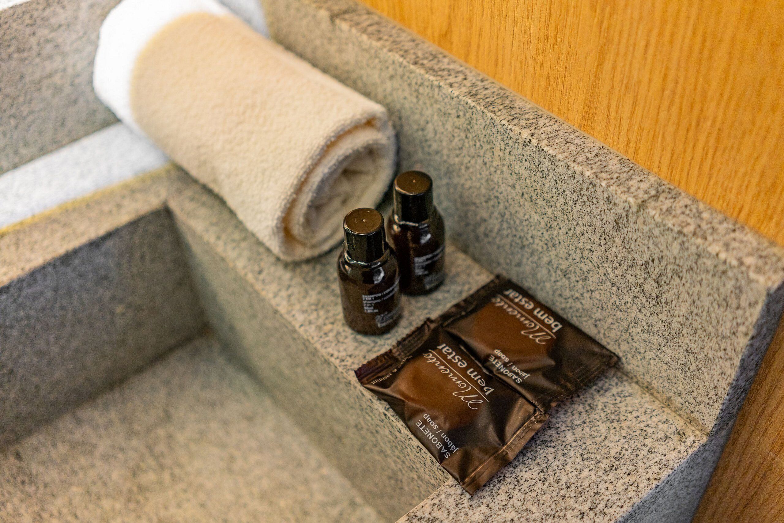 A stone ledge with a rolled towel, two small bottles, and two chocolate bars.