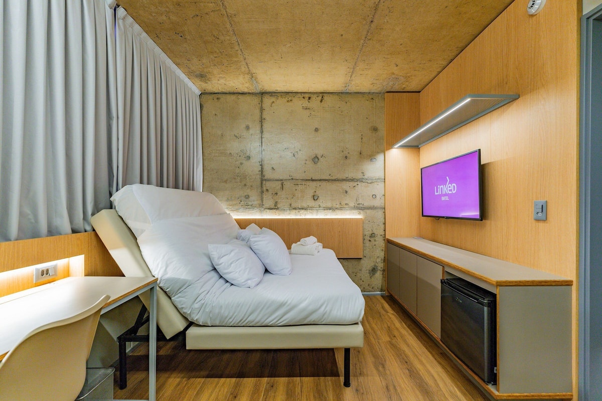 A modern hotel room with a bed, a desk, a TV, and a built-in oven.